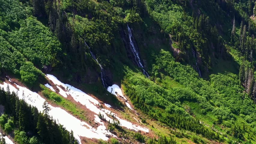 Scenic aerial shot of a small waterfall in a lush green forest on the side of a mountain in the Pacific Northwest, Washington State