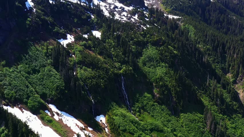 Scenic aerial shot descending and slowly zooming in on small waterfall on the cliff side surrounded by lush greenery in the Pacific Northwest, Washington State.