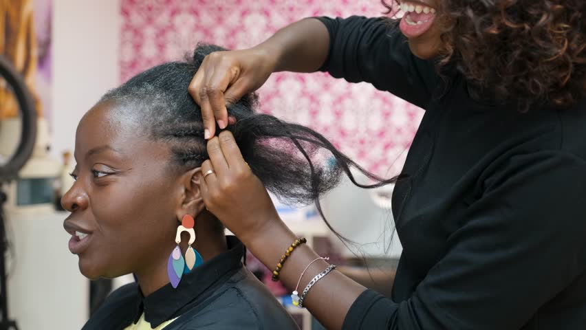 Hairdresser making crochet braids to a smiling client in an afro hair salon while talking and laughing