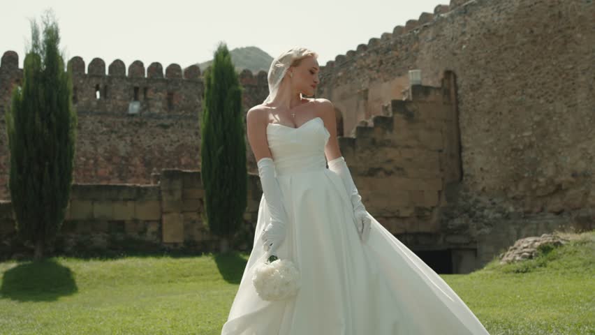 Beautiful bride with blonde hair in elegant wedding dress posing at the camera . 