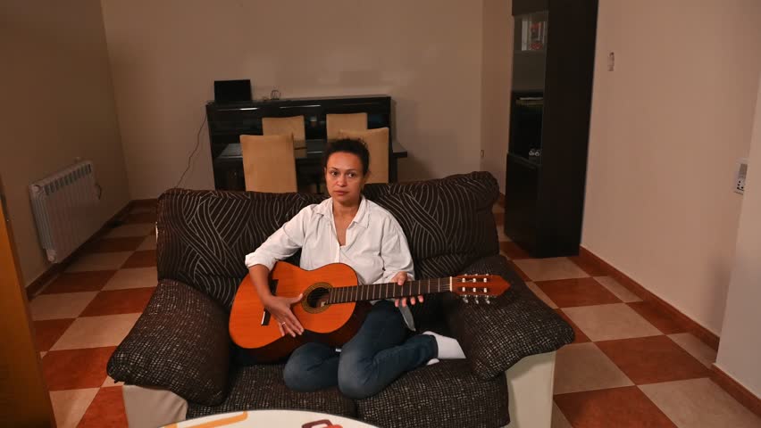 Woman playing acoustic guitar on a cozy sofa at home