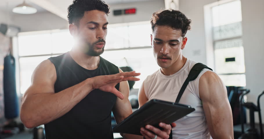 Coaching, tablet and personal trainer with people in gym for training, exercise schedule and fitness. Bodybuilder, strong and sports athlete with person and planning for energy, wellness and team
