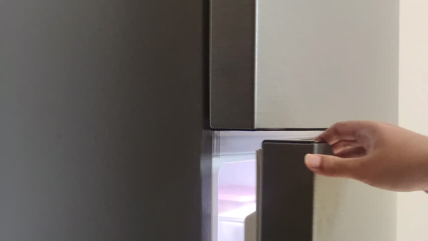 A man's hand opens and closes the doors of a gray refrigerator. Opening and closing the door of refrigerator. 
