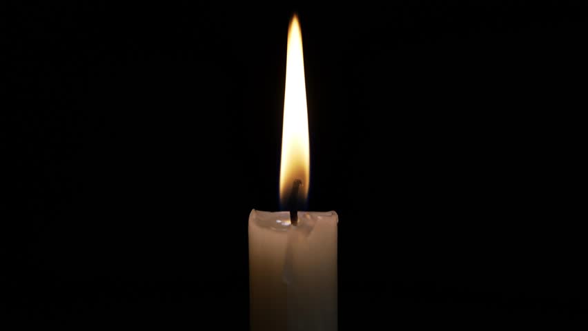 A hand strikes a match to ignite a candle in a darkened room, creating a warm glow. The flame flickers softly, illuminating the surrounding space.