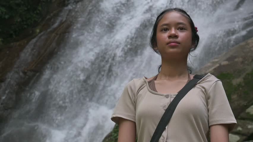 Asian young pretty girl standing and admiring the nature in tropical rainforest with big waterfall. Outdoor pursuit. Travel and Adventure concept. Ton Sung Watefall, Phang Nga, Thailand.