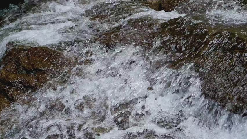 Rapid water stream flowing from cascade through the rocks under sunlight. Freshness clear water background.