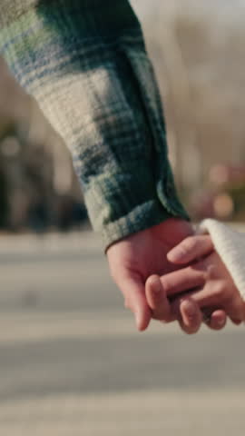 Vertical video, Close up of hands of young couple holding hands and walking down street