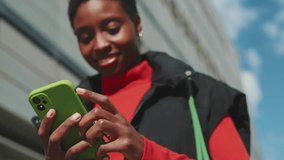 Close-up young woman with short hair dressed in warm clothes in bright sunlight standing a city street typing sms text on mobile phone, focus on phone - Powered by Shutterstock - Get 15% off with code: PIKWIZARD15