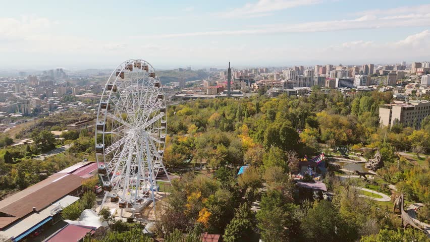 Yerevan, Armenia - 19th october, 2024: Aerial panoramic view ferris wheel in Victory Park with cityscape and buildings of Yerevan. Sunny autumn day carousels day out things to do concept