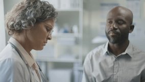 Caucasian female doctor with grey hair discussing medical documents with Black male patient during clinic appointment. Rack focus - Powered by Shutterstock - Get 15% off with code: PIKWIZARD15