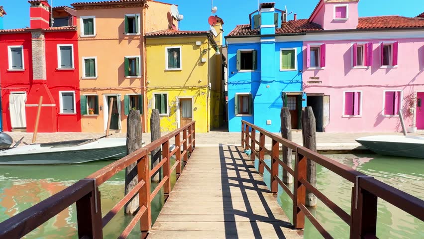 Colorful architecture in Burano island, Venice, Italy. Walking on the bridge over canal with boats. Red, pink, yellow and blue painted houses. Famous travel destination
