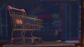 Modern economics. Business concept of securities trading. A small shopping cart from a supermarket stands against the background of a computer monitor on which economic data is changing. Close-up. - Powered by Shutterstock - Get 15% off with code: PIKWIZARD15