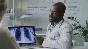 African American male doctor explaining chest X-ray on laptop to grey-haired female patient, discussing diagnosis and recommending treatment options during medical consultation in clinic - Powered by Shutterstock - Get 15% off with code: PIKWIZARD15