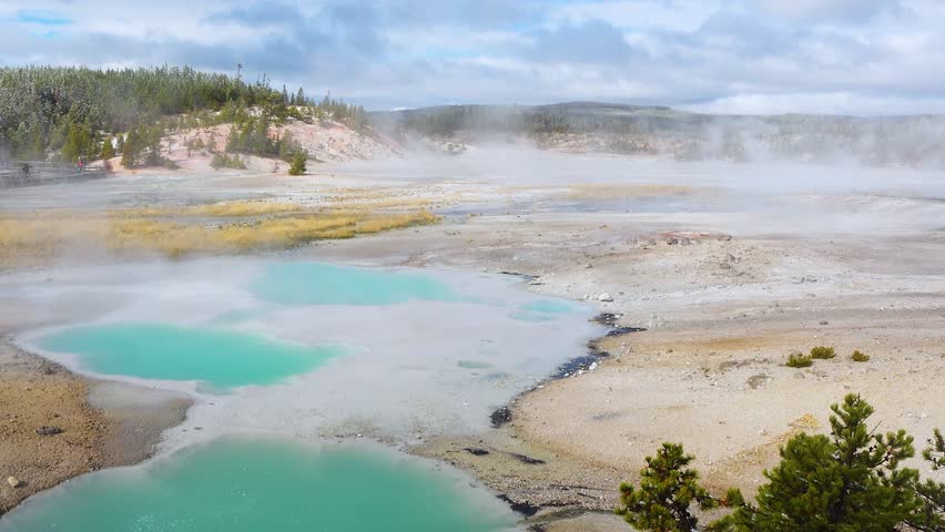 Geothermal formations and colorful pools at Yellowstone National Park, as steam rises and creates a mystical ambiance on a cool autumn day.