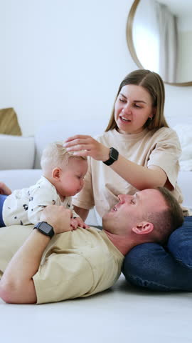 Lovely infant baby with blond hair lies on the father's chest. Mom sits beside watching and smiling. Happy family leisure time. Vertical video.