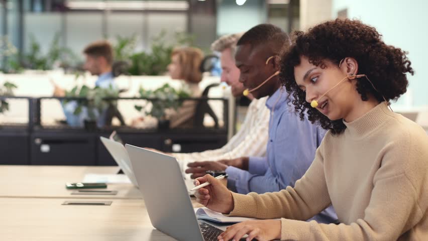 Focused female call center agent assisting clients online, providing professional support in modern office workspace