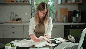 Worried woman calculating domestic bills and counting remaining money. Stressed woman sitting at kitchen table and planning personal finance. Concept of rising costs in households - Powered by Shutterstock - Get 15% off with code: PIKWIZARD15