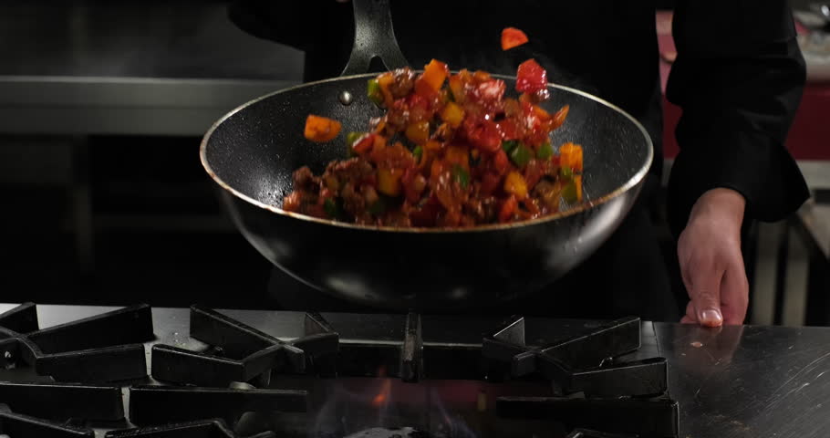 Wok pan with flying ingredients. Chef throws meat and vegetables in the air. Slow motion