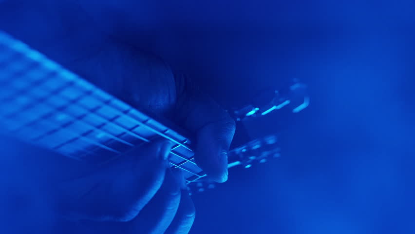 Vertical video. Acoustic concert. Guitar player. Pop event. Music stage performer man hands improvising with chords on string instrument at night show in colorful neon light smoke.