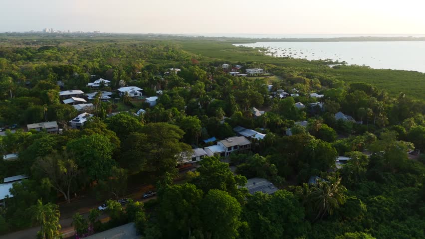 Aerial drone of green suburb in Darwin, NT, showcasing residential homes and leafy streets at sunset, light over ocean