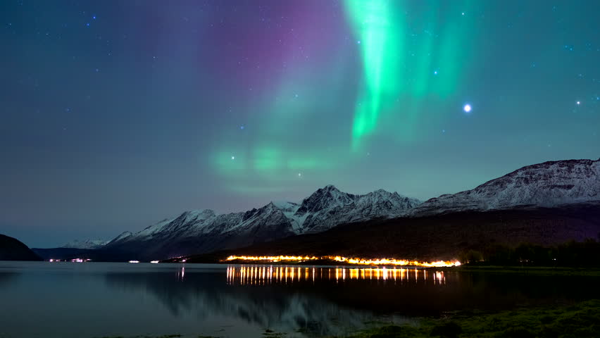 Stunning vivid aurora borealis flaring in sky over snowy mountains, nightlapse