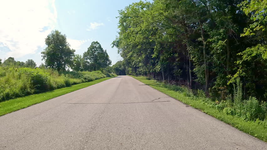 POV - driving on paved road thru Jester County Park in the Des Moines River Valley in central Iowa; driving past the one of the trailhead parking areas and a large meadow; vacation, holiday