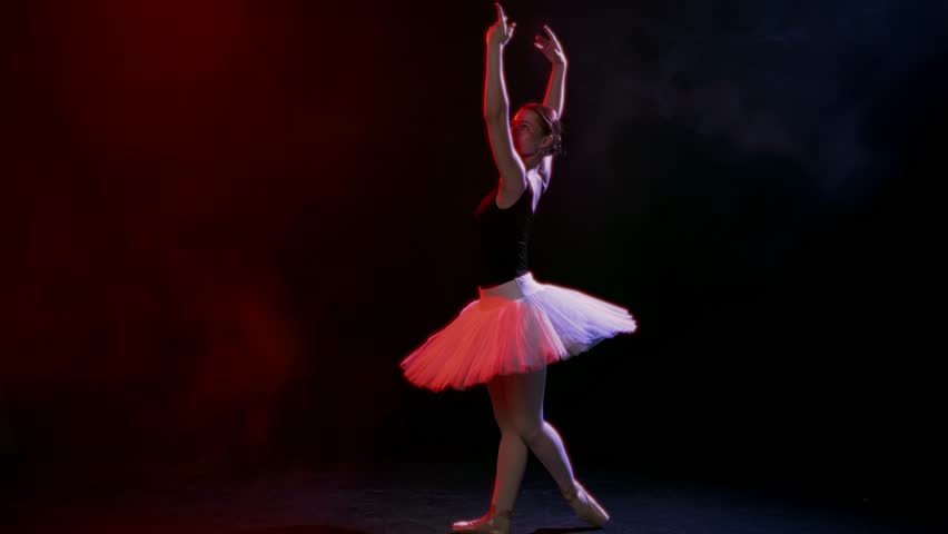 School of arts, young ballerina rehearsing in rehearsal room, slow motion shot. Beauty and grace of female ballet dancer, pretty woman in white tutu dancing alone in dark studio with artistic lighting