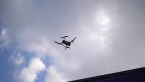 Ground view of small gray drone with four propellers flying in partially cloudy blue sky on sunny summer day, capturing aerial footage. FPV drone flying in blue sky. Shooting in slow motion. - Powered by Shutterstock - Get 15% off with code: PIKWIZARD15