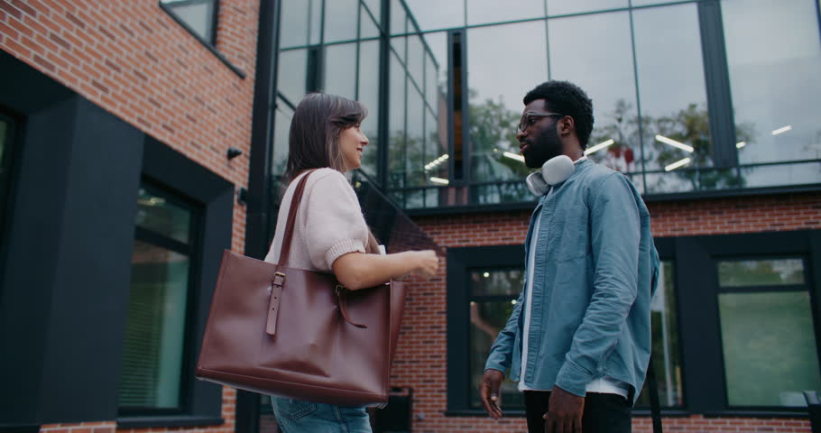 African American male standing in front of girl while answering question or explaining. Woman listening with focus. Man helping newcomer in business team with information. Supporting others.