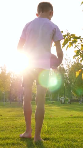 kid silhouette running with hand rugby ball. kid game american football. greenery golden hour park. short vertical. kids play ball in park