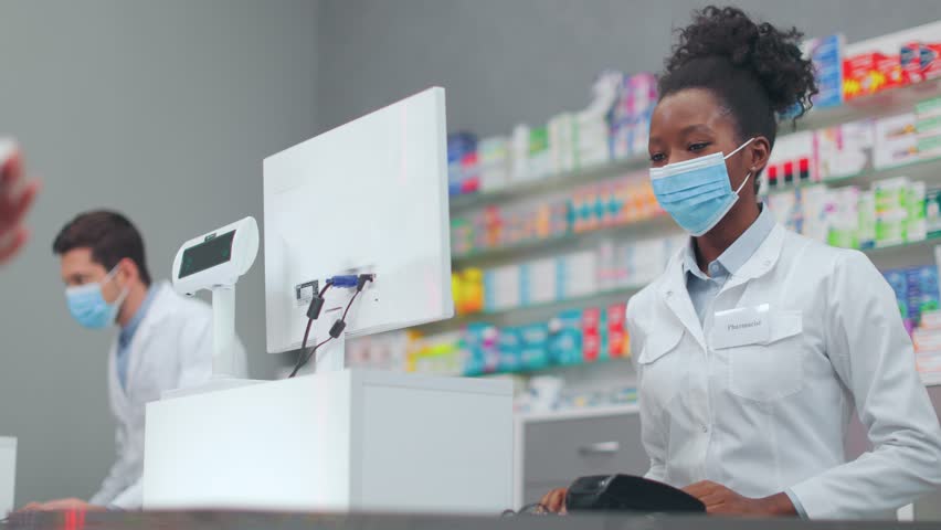 Female customer conducting non cash payment by card. African American woman pharmacist giving out medicine for customer. Client paying for drugs via terminal payment. Seller and buyer.