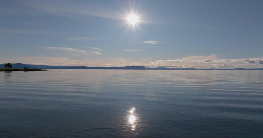 Flying low over Lake Taupo with bright sunlight reflecting on the calm water, New Zealand.