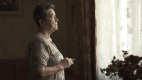 Thoughtful sad elderly woman looking out window holding handkerchief in hands. - Powered by Shutterstock - Get 15% off with code: PIKWIZARD15