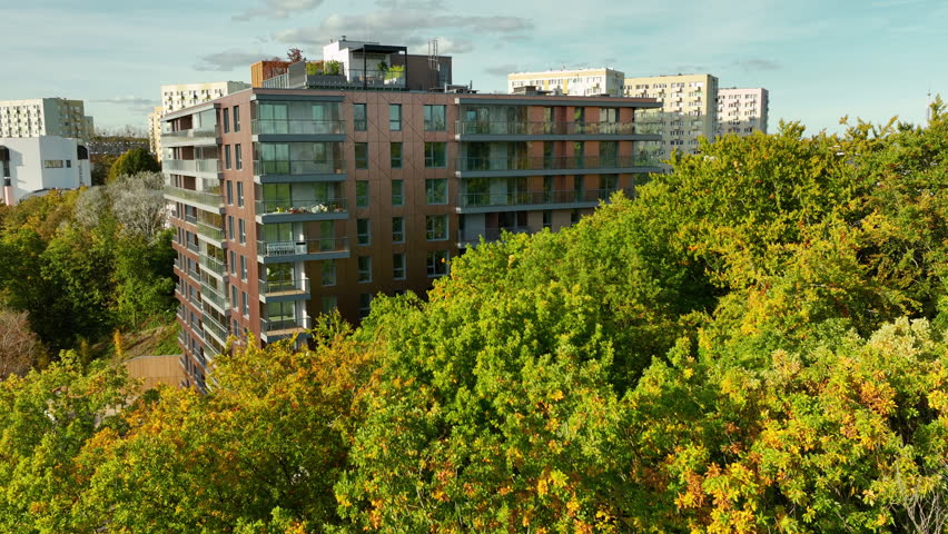 Modern apartment building surrounded by autumn trees, blending urban living with nature. High-rise residential area in Gdynia’s forested surroundings