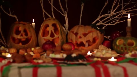 A girl in a costume of ghost is lighting the candles inside the pumpkins,then looks at the camera.