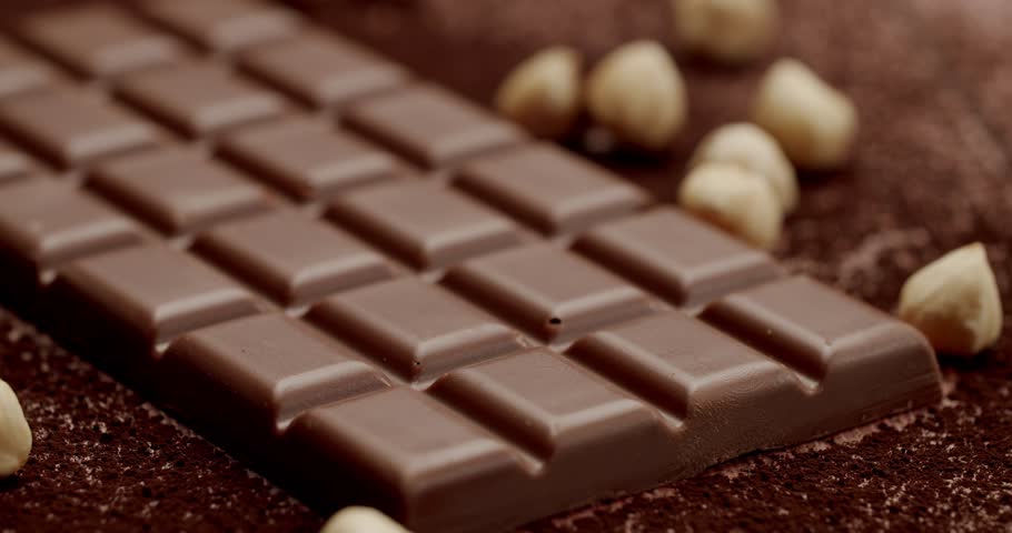 Close-up of a delicious milk chocolate bar surrounded by hazelnuts on a dark cocoa background. Perfect for themes related to sweets, desserts, and nuts. Delicious Milk Chocolate Bar with Hazelnuts