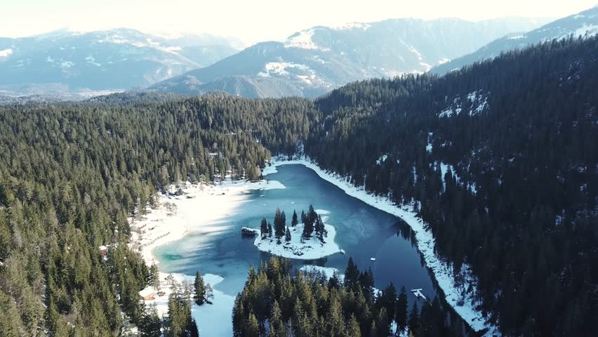 drone pull out shot of Cauma Lake or Caumasee and its small island in the middle,fwith crystal blue frozen water in beautiful mountain landscape scenery at Flims, Graubuenden - Switzerland