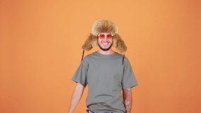 The young man, wearing a fluffy hat and funny pink glasses, playfully waves a stack of American dollars like a fan before tossing them into the air, enjoying his moment as a millionaire - Powered by Shutterstock - Get 15% off with code: PIKWIZARD15