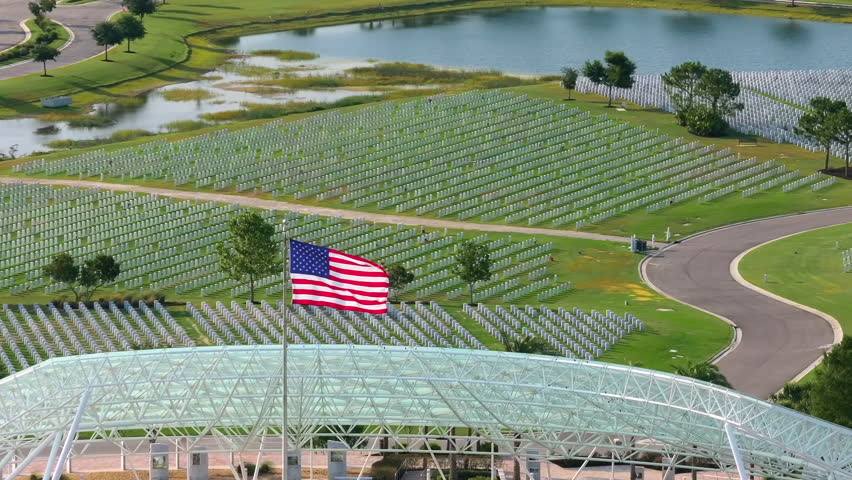 Memorial Day concept. Sarasota National Cemetery with rows of white tomb stones and USA flag on green grass.