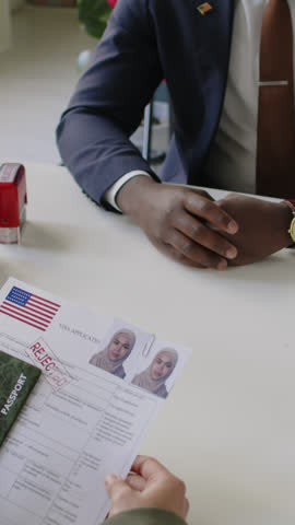 Vertical Over shoulder shot of Muslim woman in hijab taking rejected visa application form from Black male consul in US embassy