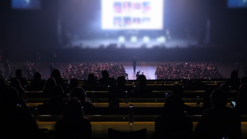 Coach's speech in front of a packed hall. A conversation about success, motivation and a future in the world. Viewers taking notes on their phone