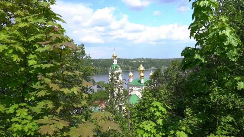 A view of a city with a church and a river in the background. The trees are green and the sky is blue