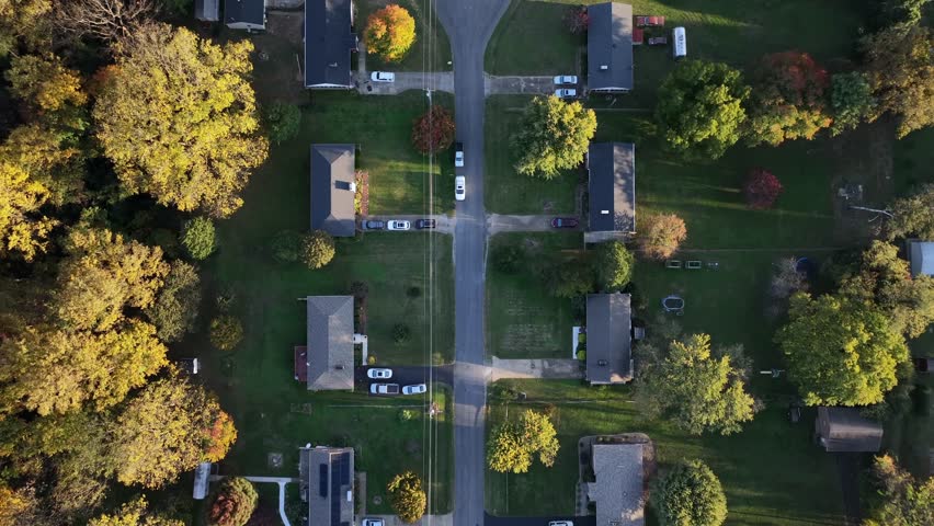 Large Villas and mansions in american suburb district at sunset time. Straight street with colorful trees on foliage autumn day. Aerial top down flyover.