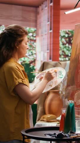 Vertical Video In a rustic workshop, artist mixes a variety of watercolor paint on palette to create a colorful masterpiece on canvas. Woman painting with a brush and showing her skill, artwork