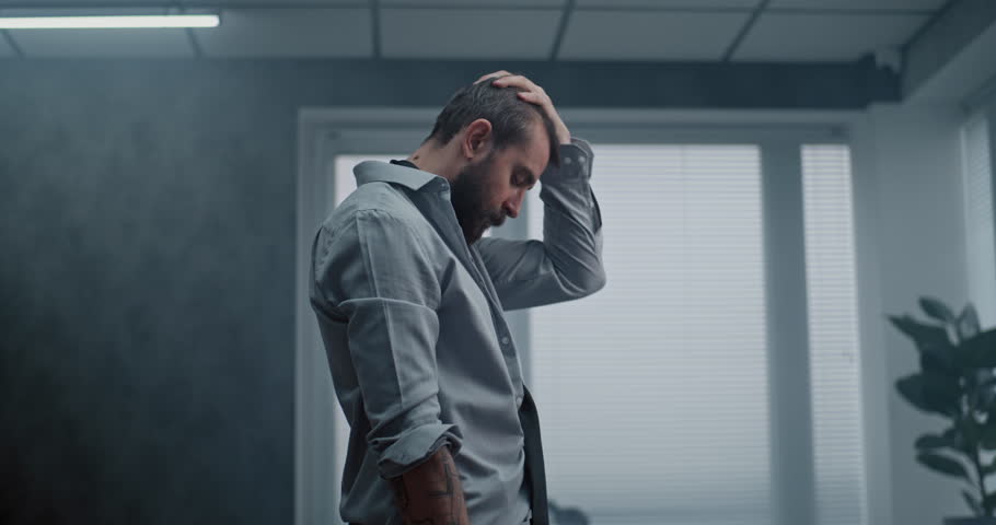 Frustrated and nervous office worker stands, breathes heavily after destroying office room. Stressed businessman after unsuccessful business deal or receiving bad news. Financial loss. Job burnout.