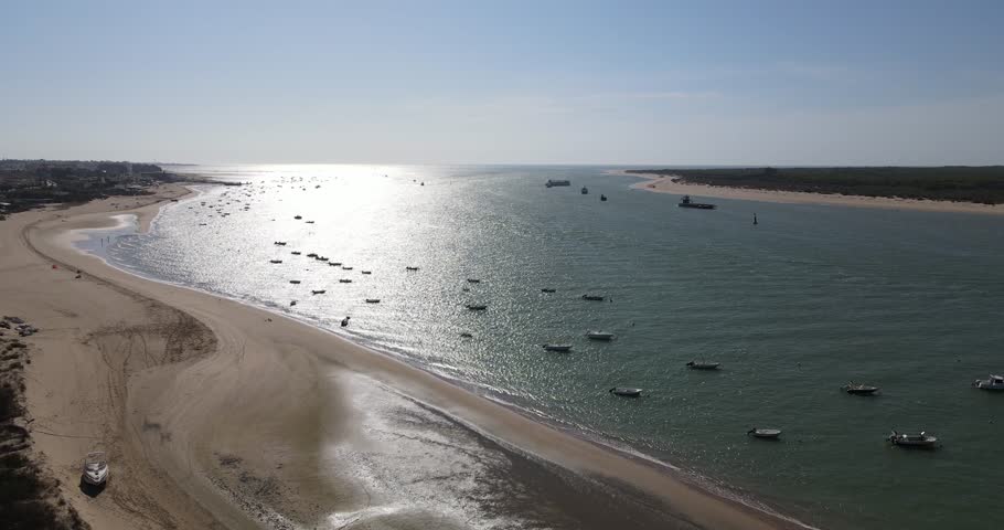 Drone footage of Bonanza beach, at the mouth of the Guadalquivir river. There are small fishing boats on the shore and in the background you can see the Doñana Natural Park.
