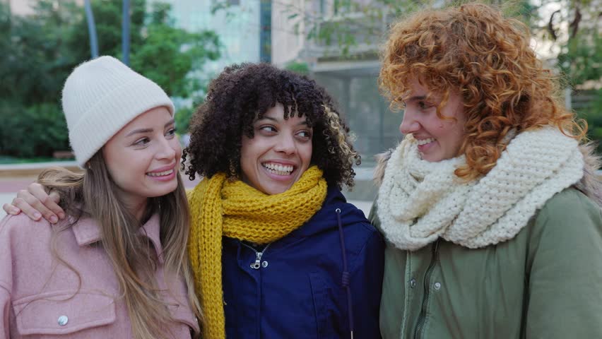 Three happy young teenage girls having fun hugging each other at city street, bundled up in cozy warm clothes. Youth and female friendship concept