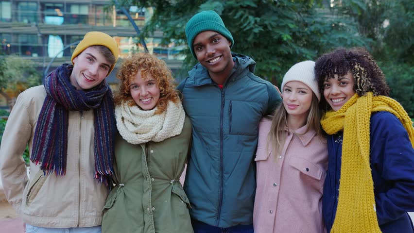 Young happy group of diverse friends in warm clothes smiling at camera standing together outside. Portrait of millennial people enjoying winter vacation. Friendship and youth concept.