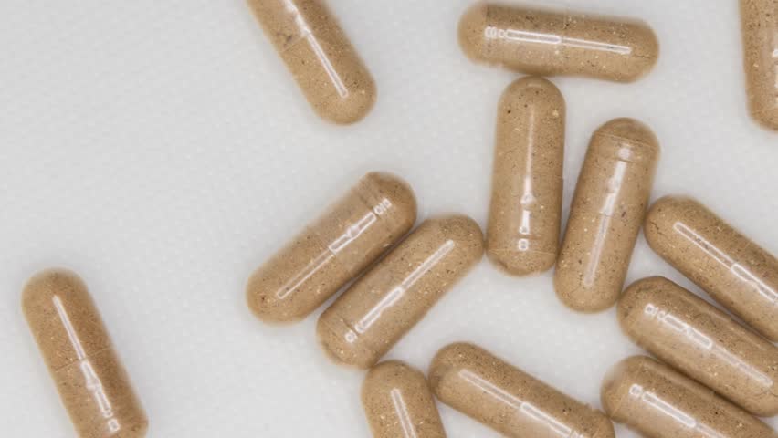 A top view of Brown herbal supplement capsules spilling from a bottle onto a white surface