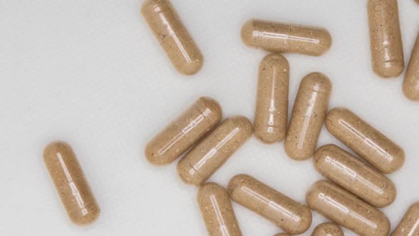 A top view of Brown herbal supplement capsules spilling from a bottle onto a white surface